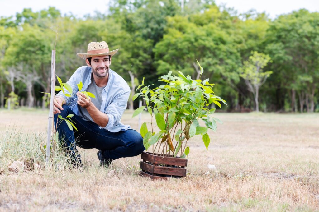 a-farmer-in-a-straw-hat-smiles-while-holding-a-young-plant-in-a-field-.jpg